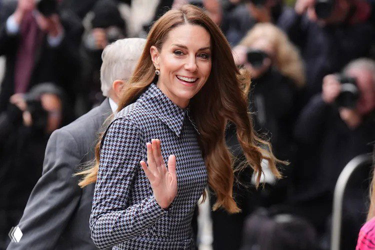 Женщина в платье в ломаную клетку машет рукой публике на входе в здание, вокруг фотографы и люди, портретный план головы и плеч