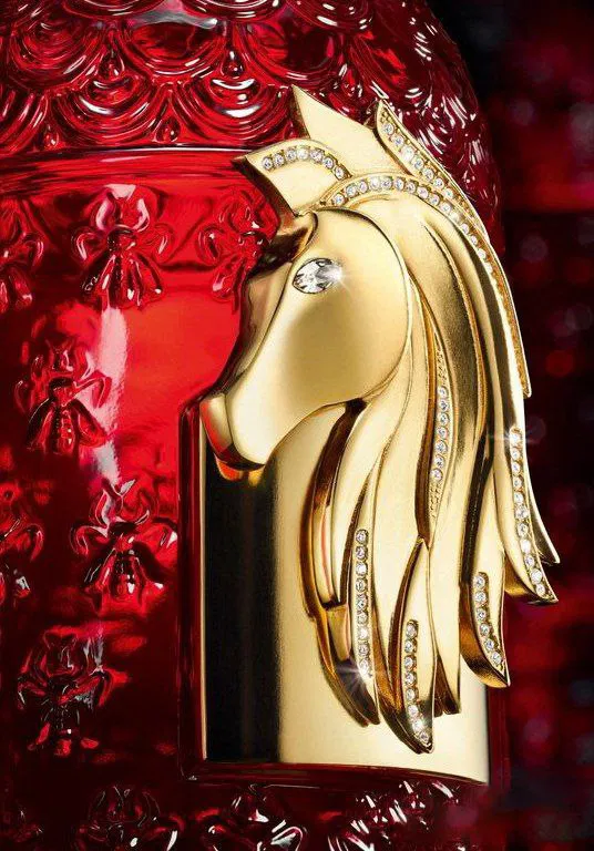 Крупный план золотой фигурки лошади на флаконе Rouge Voluptueux: ювелирная деталь с гривой и инкрустацией кристаллами.