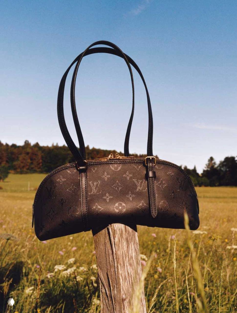 Черная сумка Louis Vuitton с длиными ручками установлена на деревянный столб на фоне поля и синего неба, лаконичный силуэт сумки.