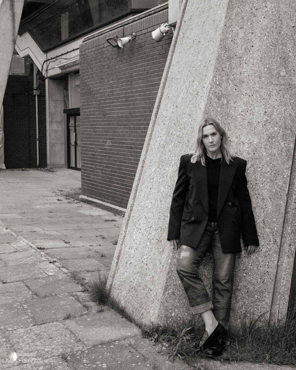 Женщина в пиджаке опирается о бетонную архитектурную колонну у универсального здания — архитектурный фон и городской пейзаж.