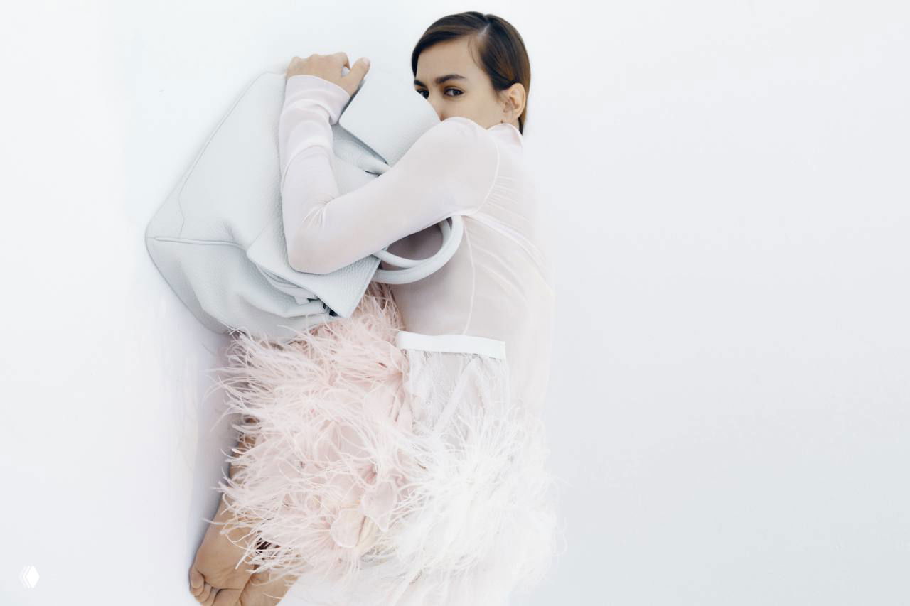 Модель лежащая у стены с крупной сумкой и перьевым элементом в образе, нежная пастельная палитра и стилизация для Marie Claire.