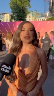 Карина Нигай на Marie Claire Blogger Party в оранжевом платье; кадр с ведущей у микрофона Marie Claire на фоне гостей и декора мероприятия.
