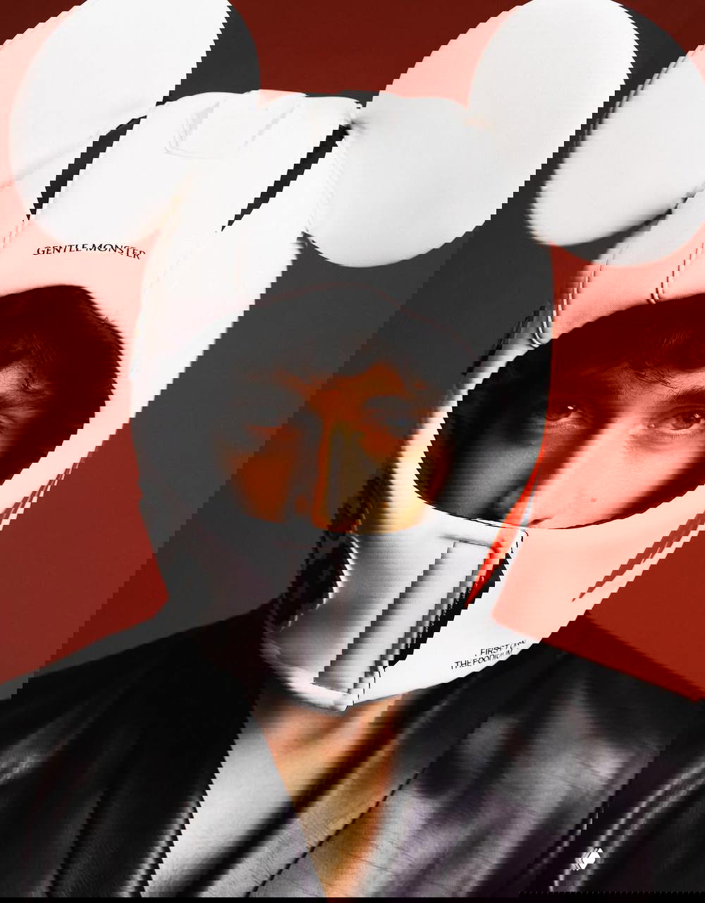 Крупный план лица модели в белом мотоциклетном шлеме с большими круглыми «ушами» на однотонном красном фоне — студийный модный кадр.