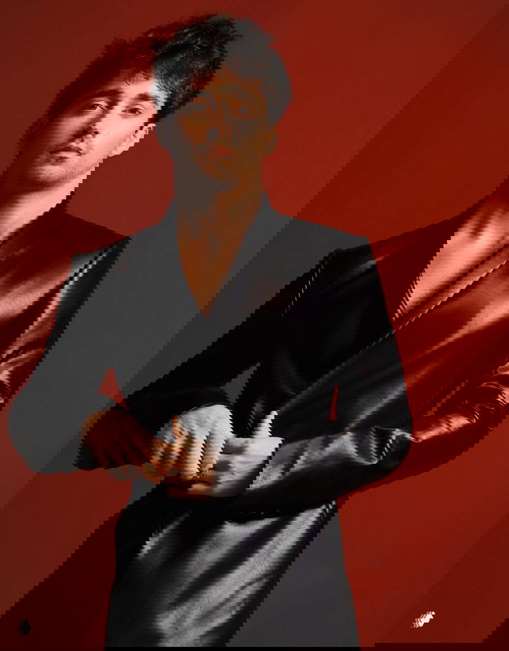 Портрет мужчины в чёрном кожаном пиджаке на однотонном красном фоне — стилизованный кадр из модной фотосессии с акцентом на силуэт и текстуру.