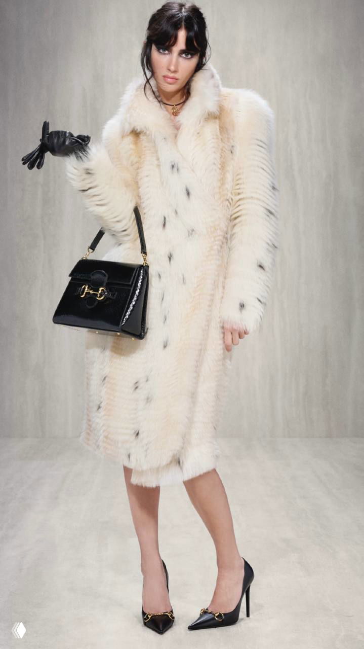 Модель в кремовом длинном пальто с черной сумкой и перчаткой, винтажный силуэт — кадр из коллекции Primavera для Gucci.