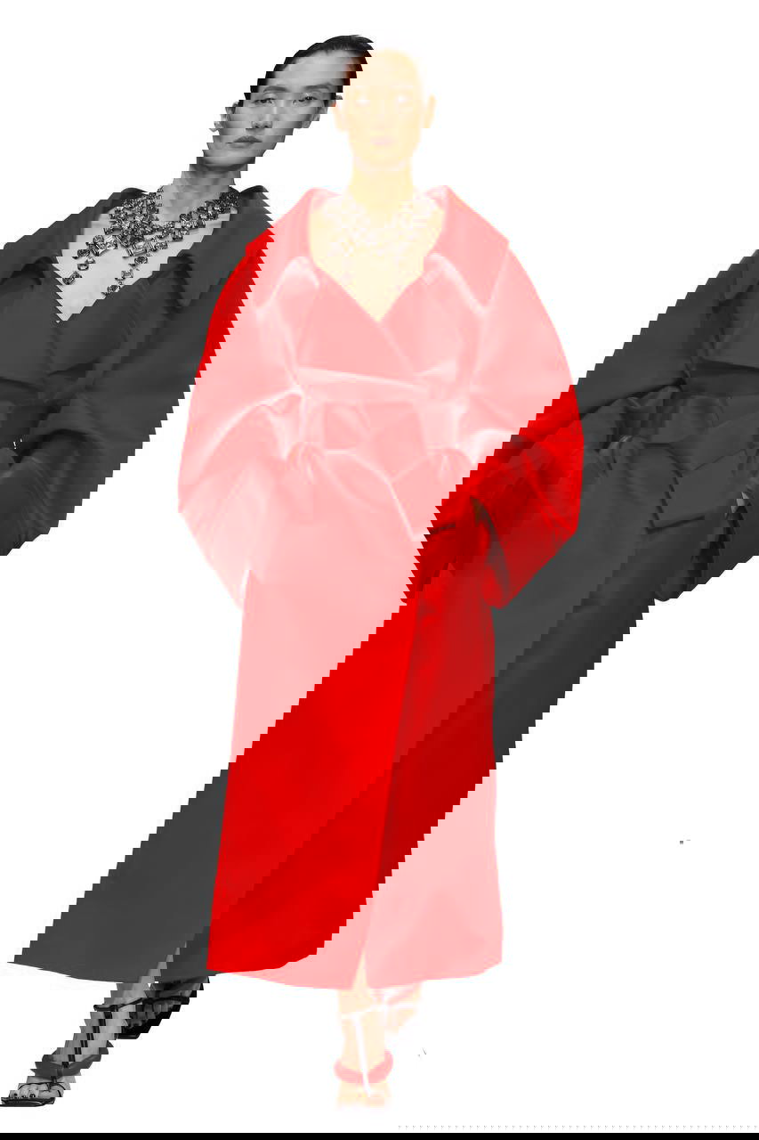 Подиумный образ: плотное алое пальто с объёмными рукавами и глубоким декольте, крупное украшение подчёркивает контраст на белом фоне.