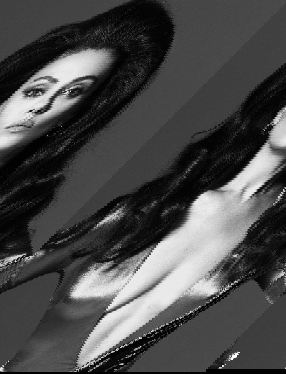 Полноразмерный портрет с пышной причёской и глубоким декольте, статичная поза и студийное освещение в чёрно‑белом тоне.