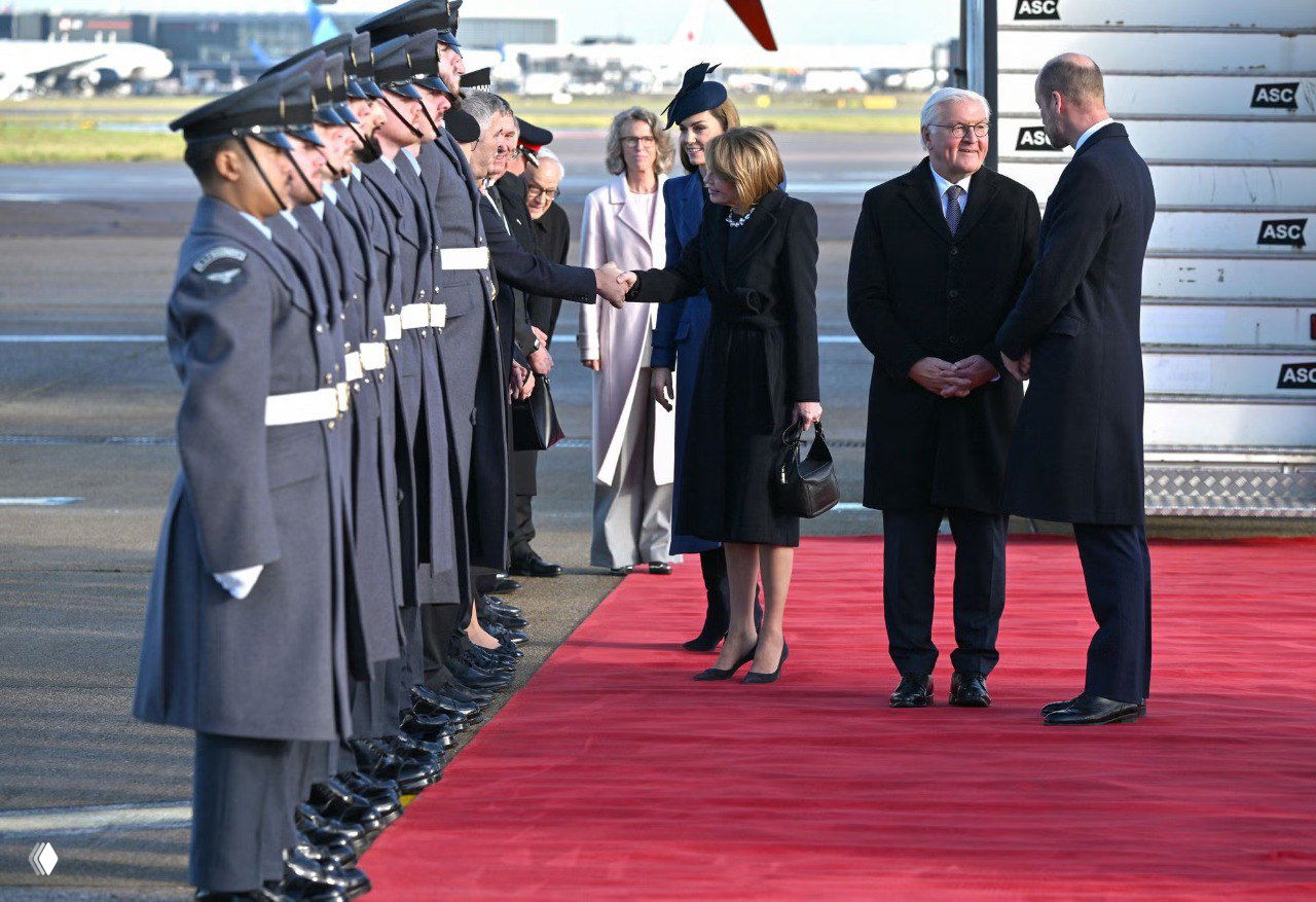 Ряд военных на красной дорожке здороваются с прибывшими гостями; видна делегация и женщины в тёмных и синих пальто.