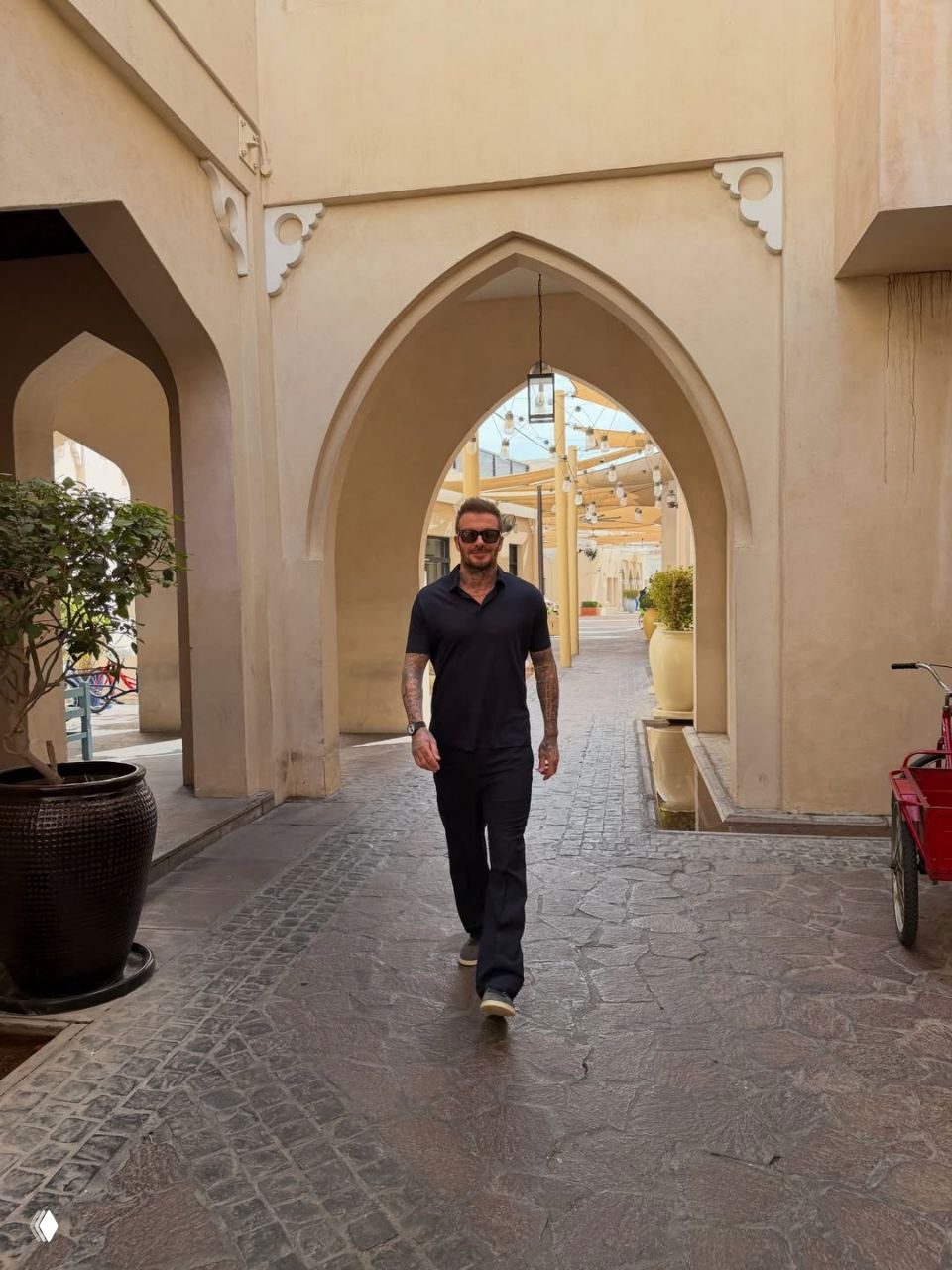 Человек в тёмной рубашке идёт по узкой улице с арочными проходами и архитектурой в стиле старого рынка в Дохе.