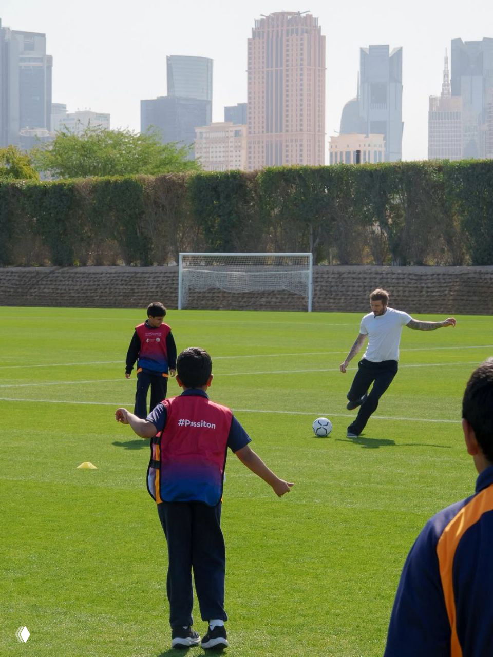 Игровая площадка: взрослый играет в футбол с детьми на зелёном поле на фоне городского силуэта и ворот.