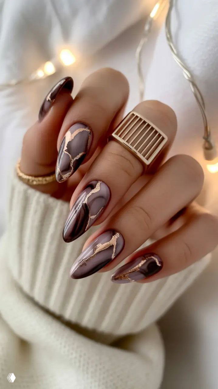 Рука с длинными ногтями в холодных коричнево‑фиолетовых тонах и декоративными золотыми «трешинками», на фоне свитера и мягкого света