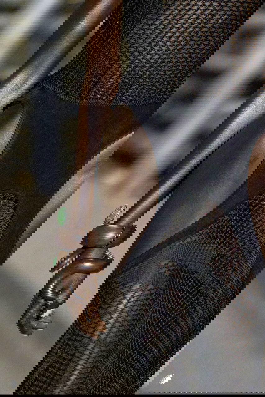 Фрагмент показа: рука модели с массивными деревянными браслетами и зелёными полудрагоценными вставками, текстура дерева и камня рядом.