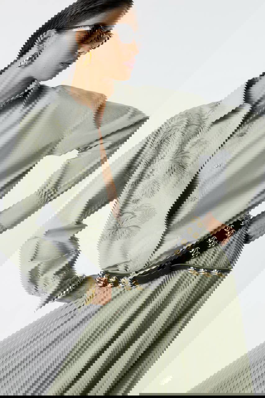 Женский образ с пудровой рубашкой и плиссированной юбкой, широкий ремень с металлическими деталями — сочетание текстур и акцентов от Liu•Jo.