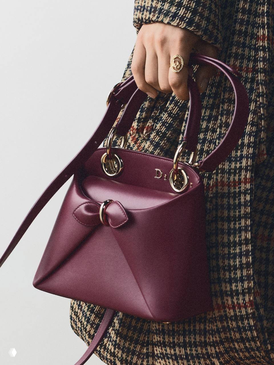 Бордовая мини‑сумка Dior Cigale в руках модели на фоне твидового пальто, видно плечевой ремень и округлые металлические крепления.