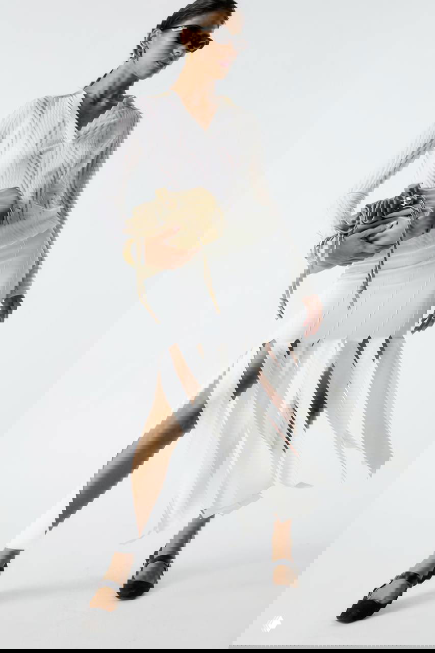 Модель в светлой верхней одежде и юбке с филированными лентами, сумка с мягкой сборкой в руках — движение и лёгкость в образе Liu•Jo.