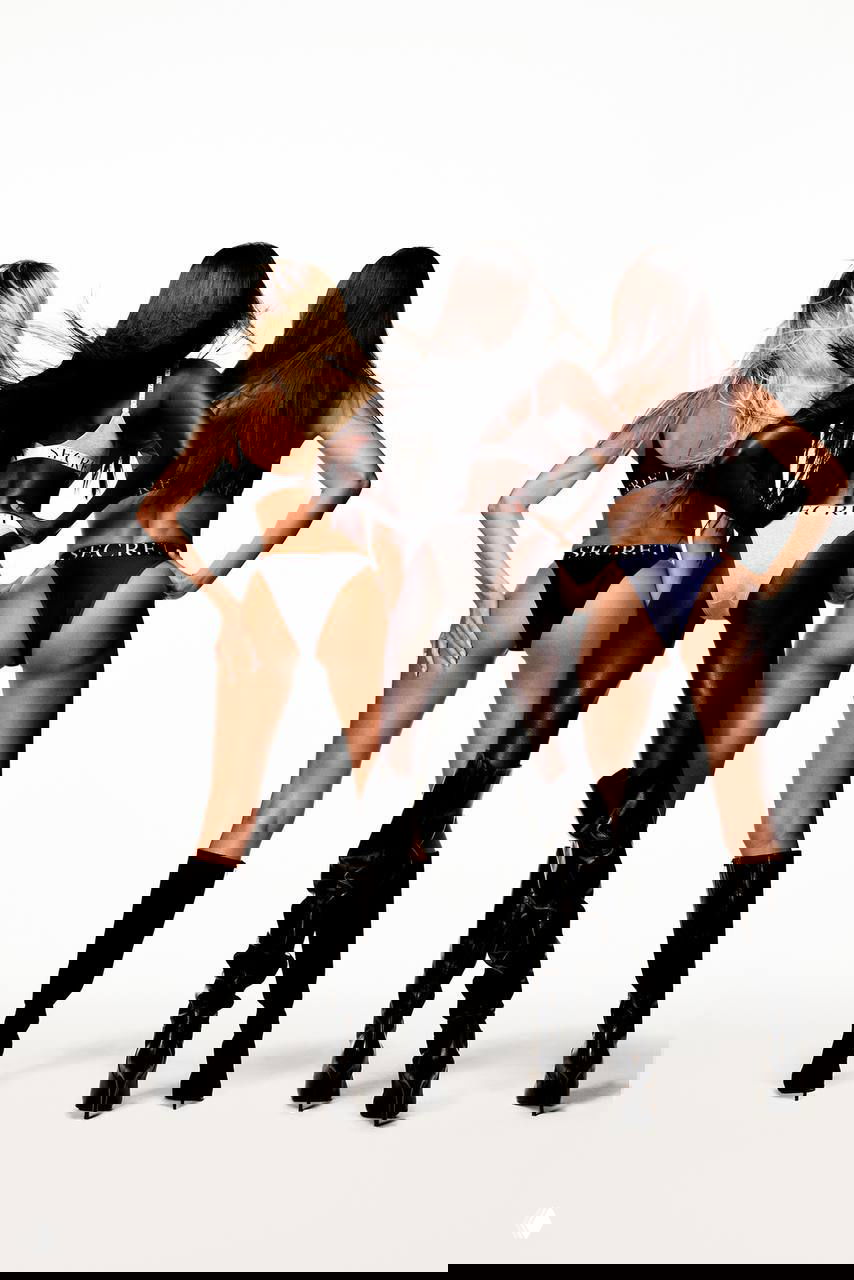 Три модели сняты со спины в бикини Victoria’s Secret — вид сзади подчёркивает брендовую ленту на поясах и сапоги.