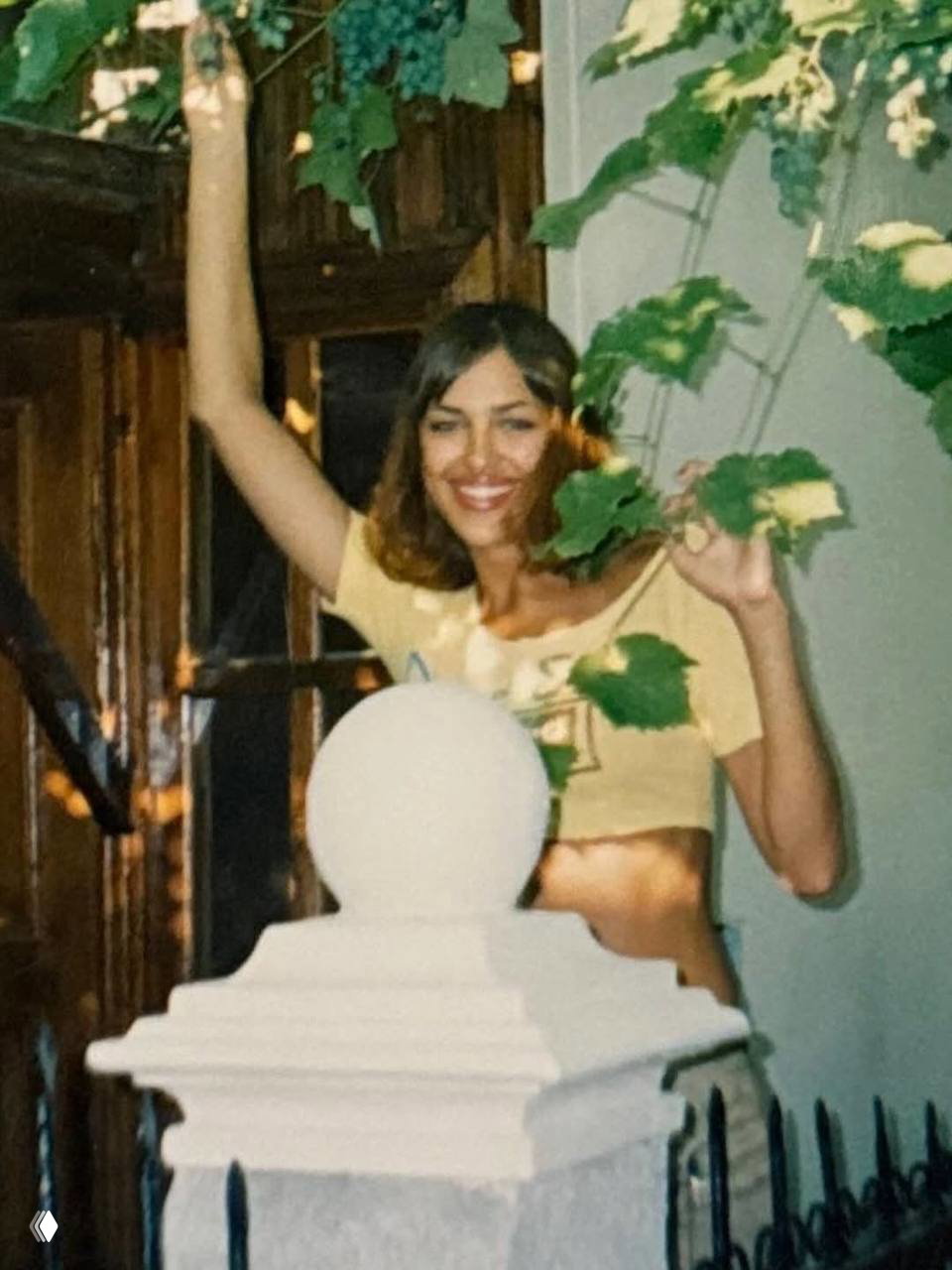 Момент радости: молодая Ирина Шейк улыбается возле листвы, в короткой футболке, похожий на летний вечер и непринужденную атмосферу.