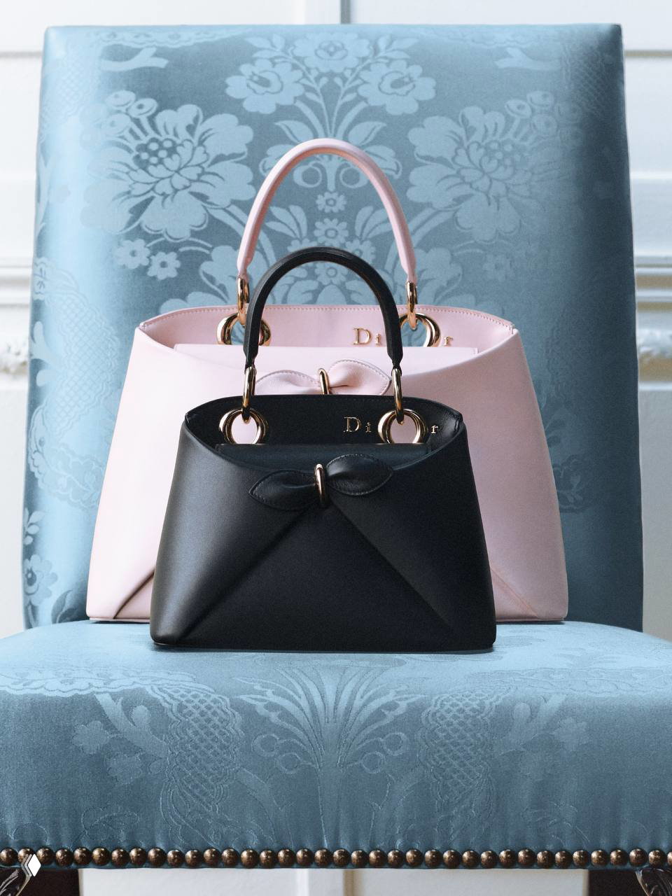 Несколько сумок Dior Cigale черного и пастельно‑розового цвета одна на фоне другой на мягком кресле, демонстрация цветовой гаммы и силуэта.