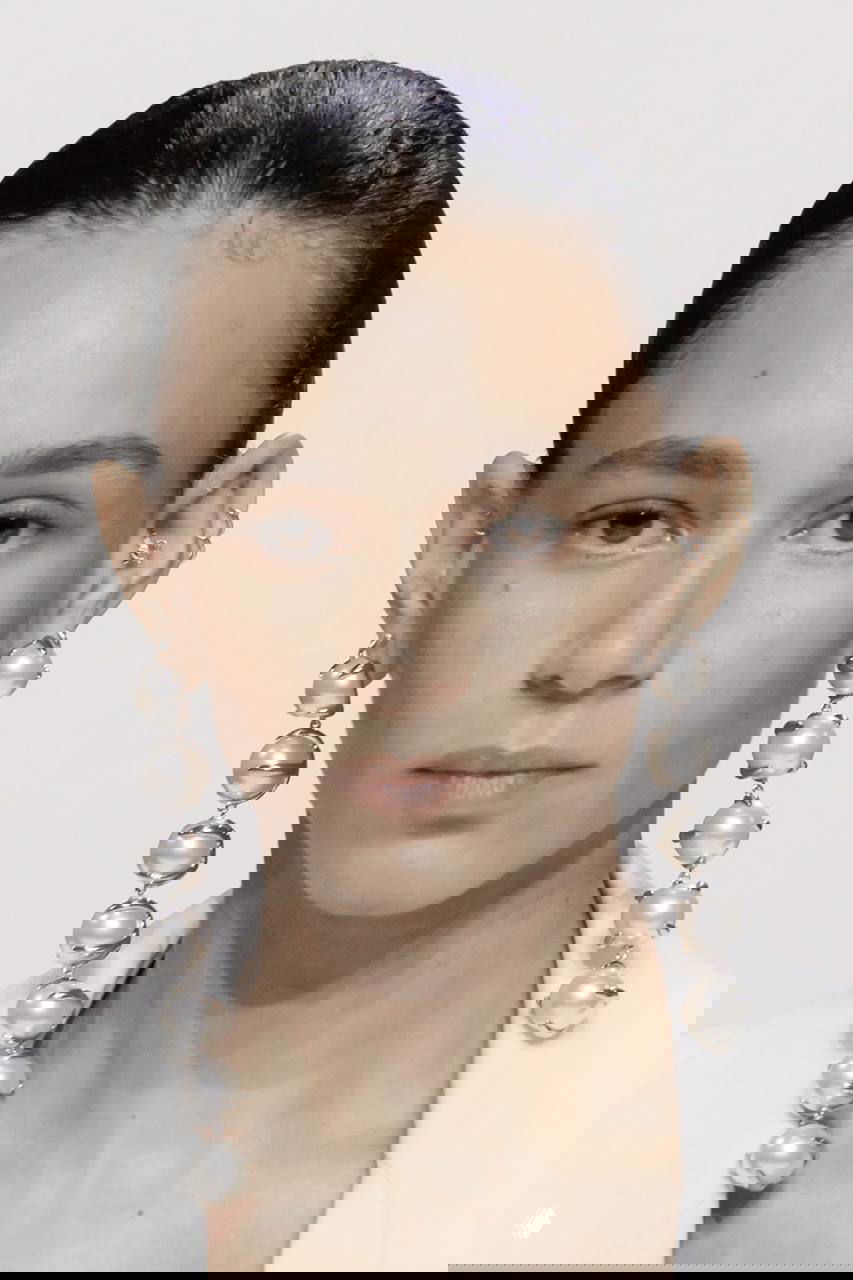 Портрет модели в гладкой причёске: длинные серьги-цепочки с крупными барочными жемчужинами, монументальный oversize-жемчуг в фокусе.