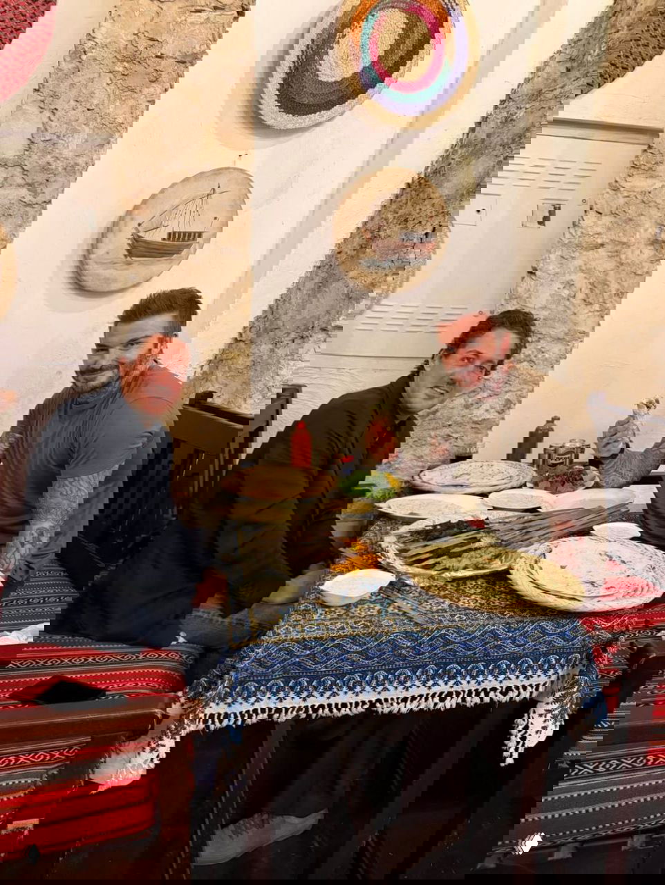 Мужчина с татуировками и собеседник едят за столом с шампурами и лавашом; атмосфера традиционного ресторана.