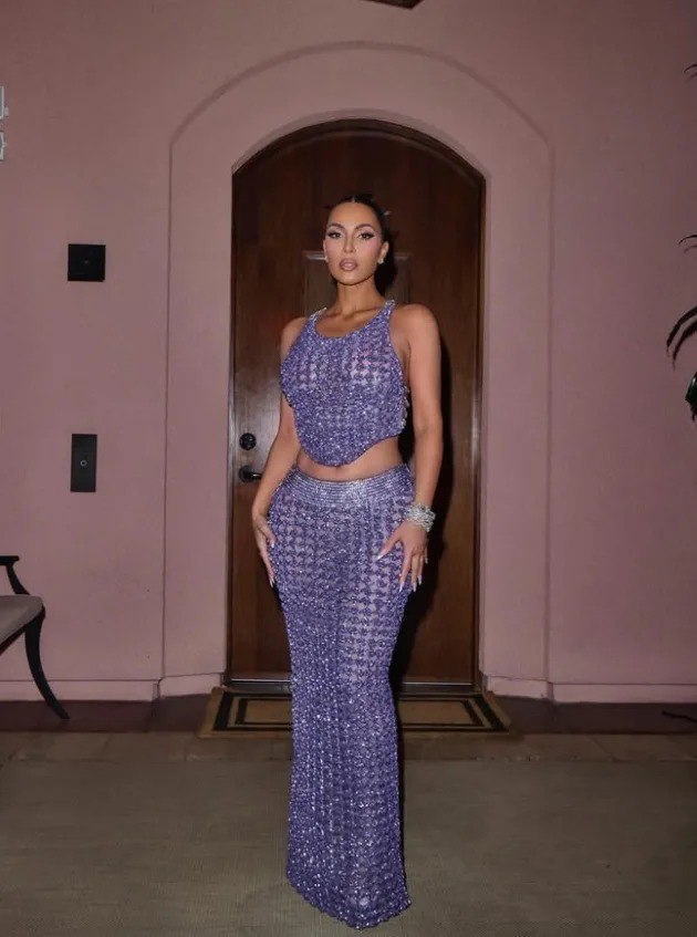 Женщина в сиреневом блестящем костюме-платье позирует у арочного дверного проёма; съёмка в помещении перед входом.