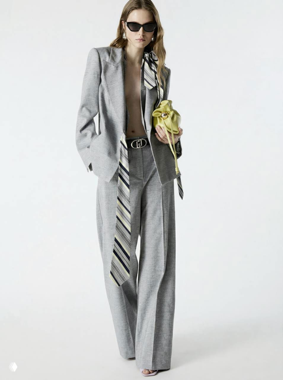 Серый костюм в мужском стиле с широкими брюками и длинным галстук-подобным аксессуаром, мини-сумка зелёного оттенка — строгая база и неожиданный аксессуар.
