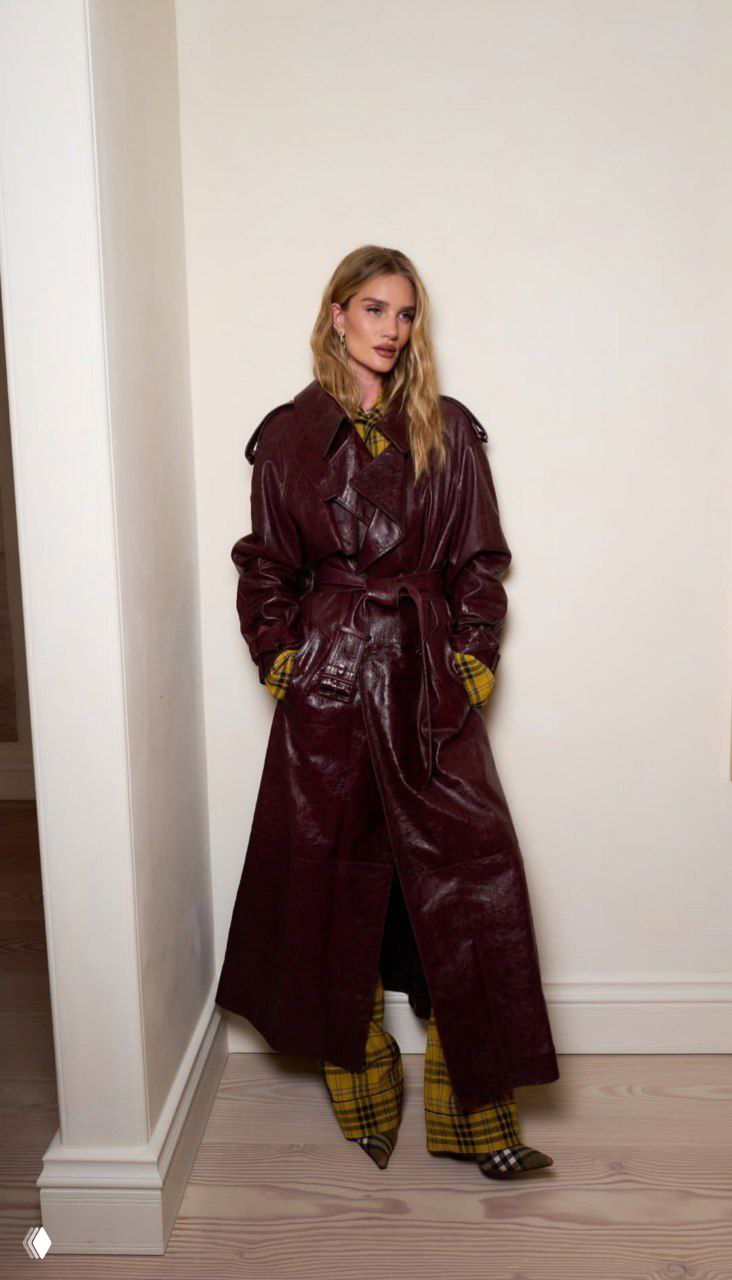 Полноразмерный портрет женщины в тёмном лаке кожаном пальто и клетчатом жёлтом костюме на нейтральном фоне студийного коридора.