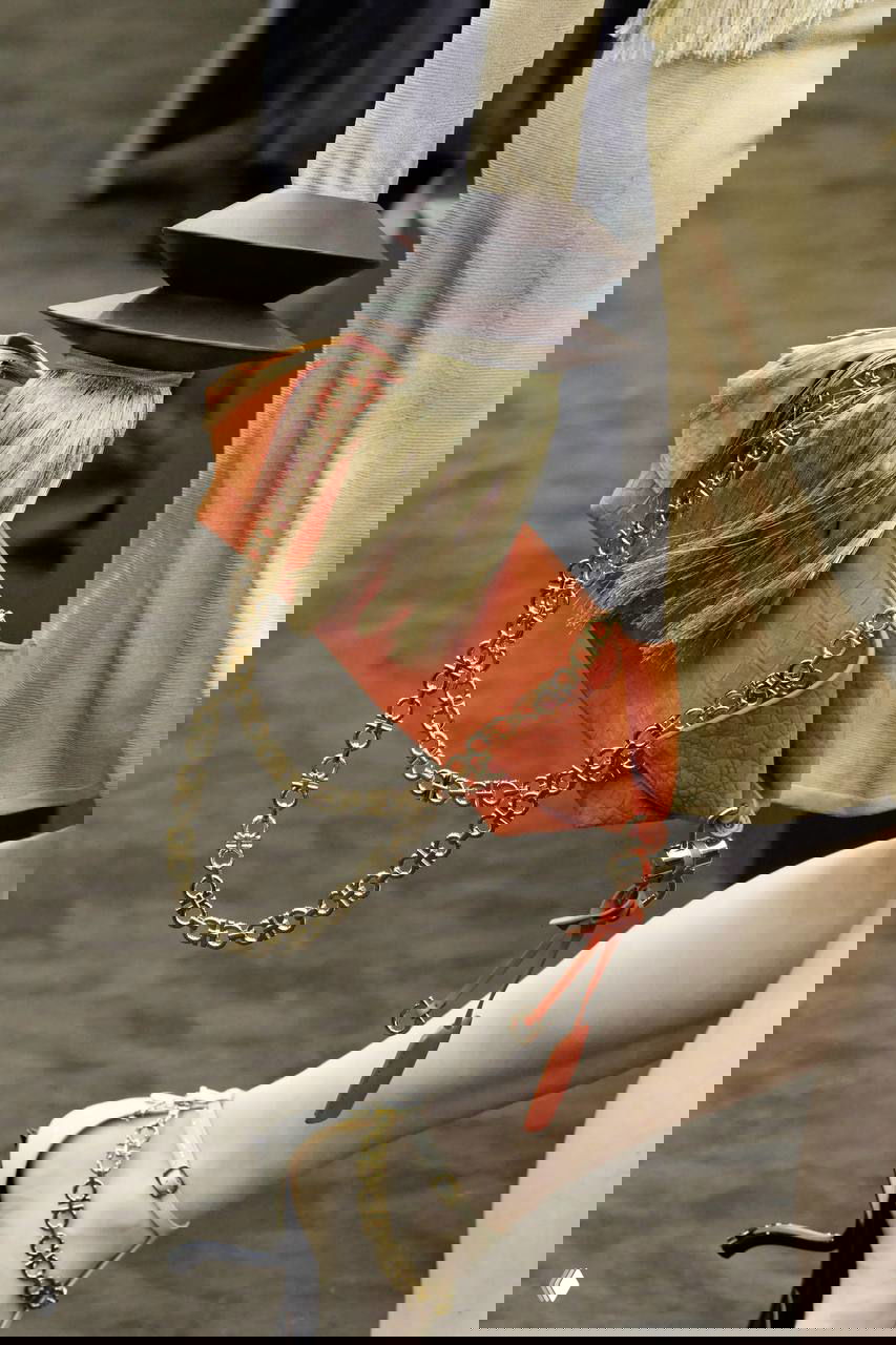 Кадр с аксессуарами на подиуме: сумка с текстурой и крупной цепочкой, декор из кистей и деревянных элементов — органичный декор образа.