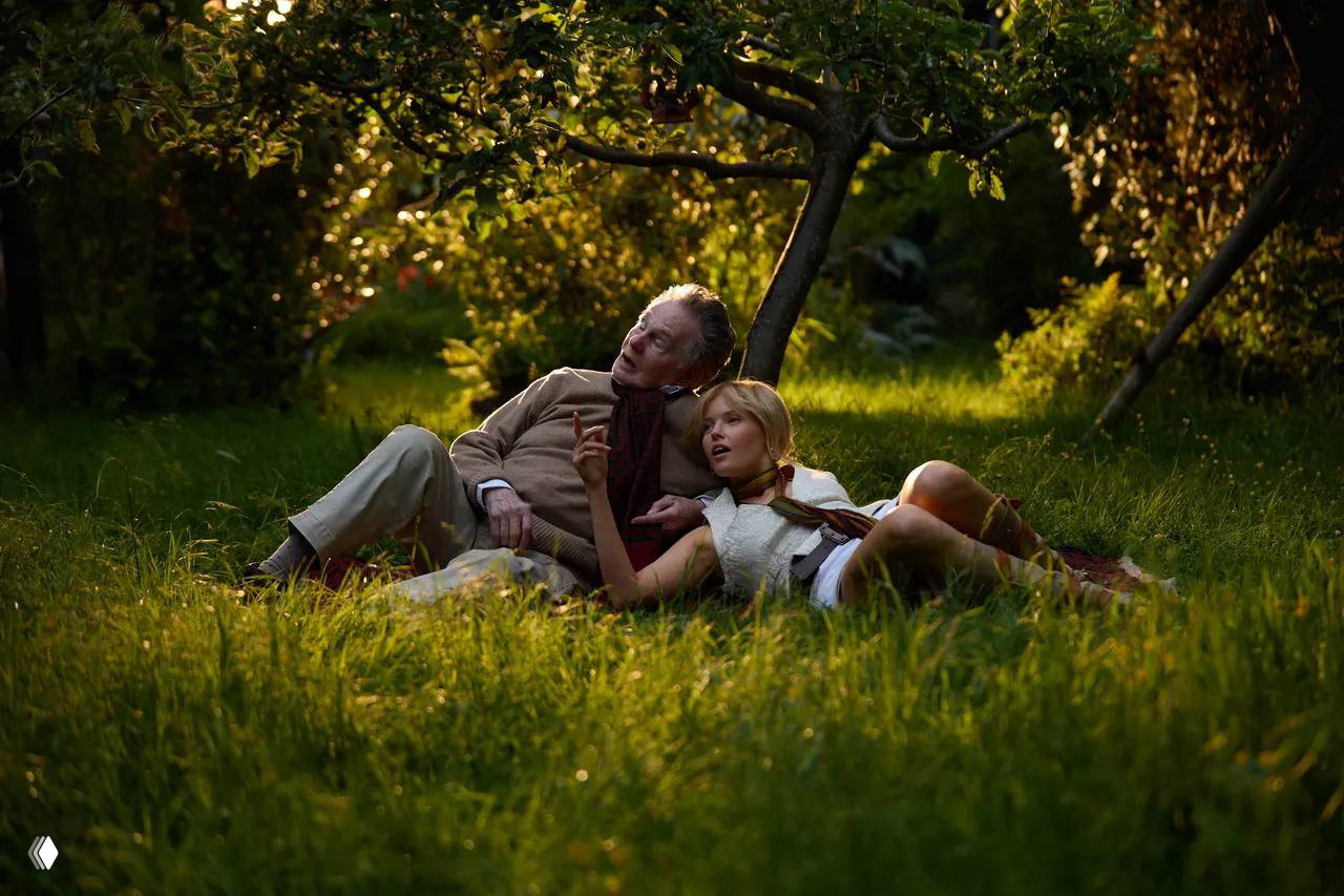 Мужчина и женщина лежат в саду на траве в романтической сцене на съемочной площадке — теплый боковой свет и естественный антураж.