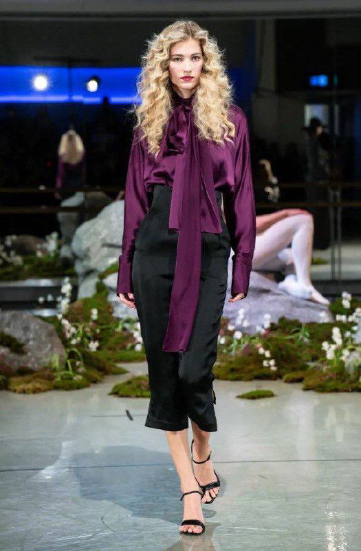 Модель в сливовой шелковой блузе с шейным бантом и чёрной юбкой идёт по подиуму дизайнера Патрика Макдауэлла на показе в Лондоне.