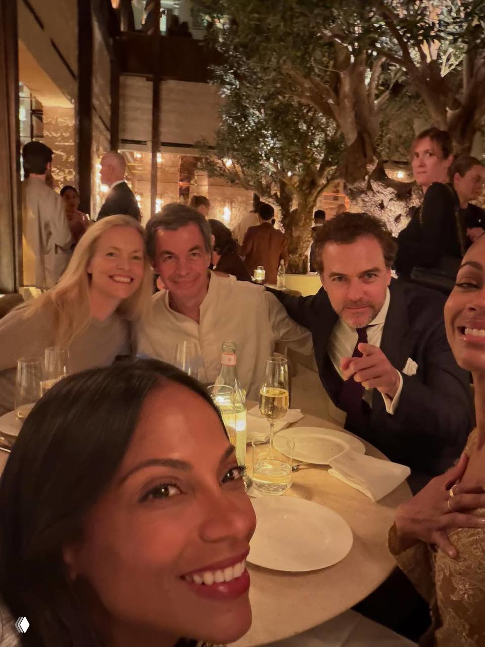 Гости ужина делают селфи за круглым столом на фестивале Fuorisalone в Милане — тёплое освещение, посуда и разговоры в непринуждённой обстановке.