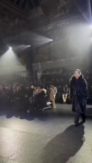 Широкий кадр показа Burberry: Роузи Хантингтон-Уайтли идёт по подиуму в меховом пальто, туманное освещение и тени зала подчёркивают атмосферу шоу.