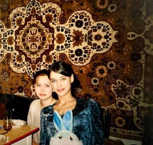 Снимок в кухонной обстановке: молодая Ирина Шейк сидит за столом с игрушкой-зайцем на коленях, на стене виден традиционный ковровый рисунок.