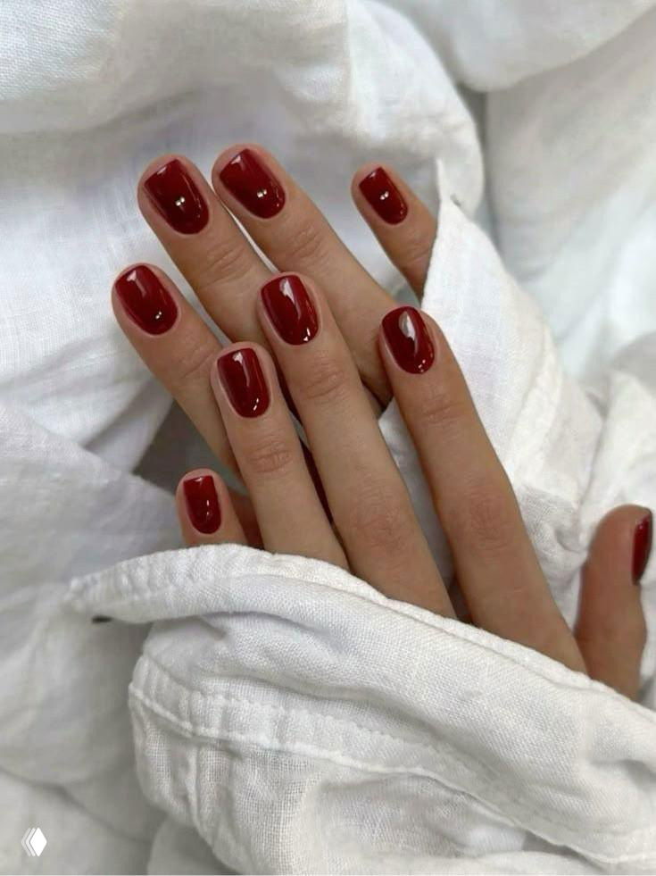 Короткие аккуратные ногти квадратной формы с насыщенно‑бордовым глянцевым покрытием на фоне белой ткани, минималистичный вариант для осени.