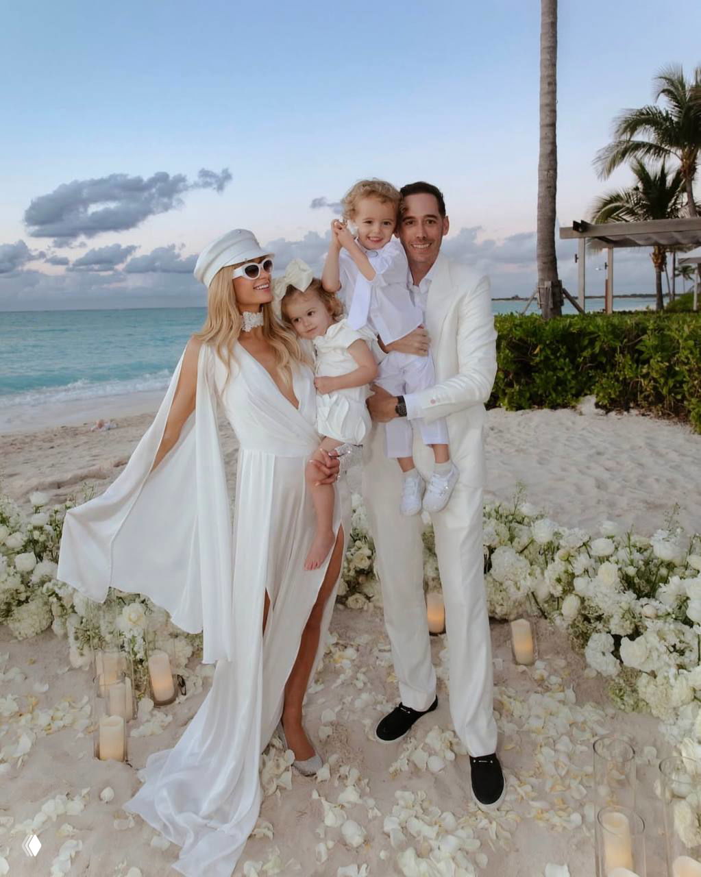 Семейный снимок Перис Хилтон и Картера Руума с детьми на берегу моря: пальмы, песок и белая стилистика вечеринки на острове.