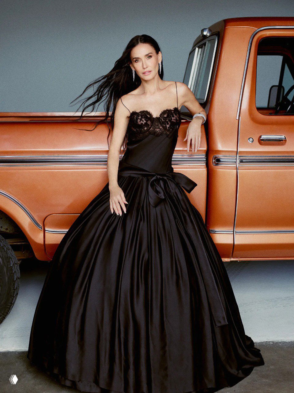 Полнофигурный кадр женщины в чёрном пышном платье, опирающейся о кузов винтажного пикапа — студийный фон и кинематографичный свет.