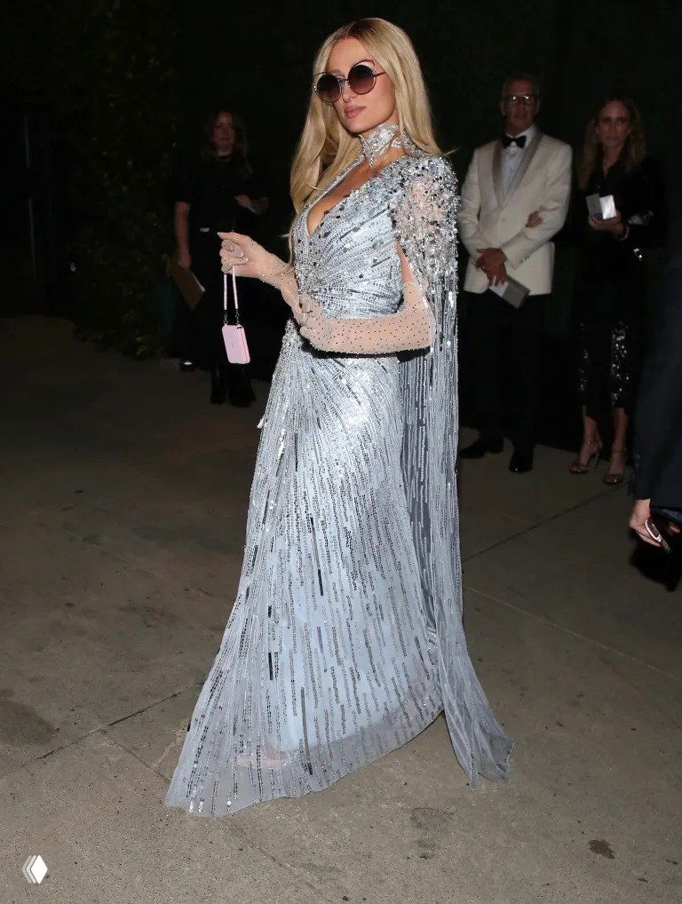 Женщина в длинном светло-голубом расшитом платье с накидкой идёт по дорожке вечера; элегантный образ для торжественного выхода.