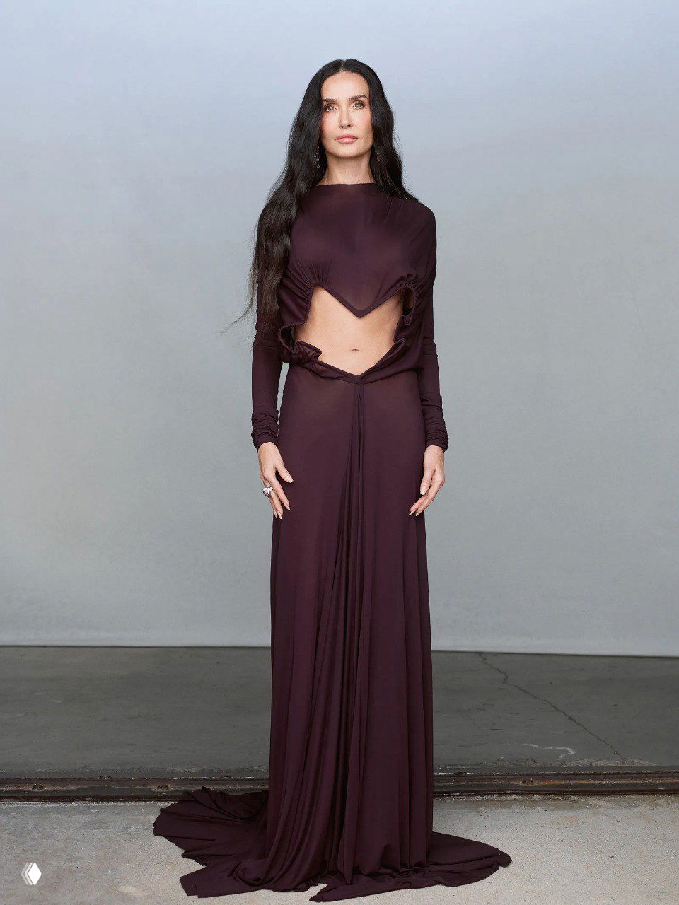 Высокая портретная композиция женщины в тёмном платье с открытым животом и длинным шлейфом на нейтральном фоне студии, сдержанный художественный стиль.