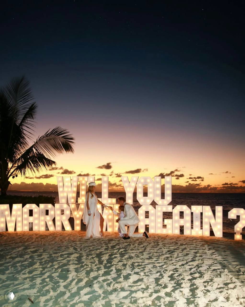 Пара позирует у больших светящихся букв с надписью предложения на берегу: драматическая инсталляция на закате дополняет атмосферу ремейка свадьбы.