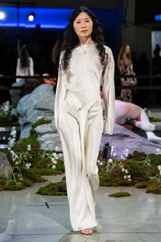 Модель в светлом струящемся костюме идёт по подиуму на показе Патрика Макдауэлла; стиль коллекции сочетает элегантность и минимализм.