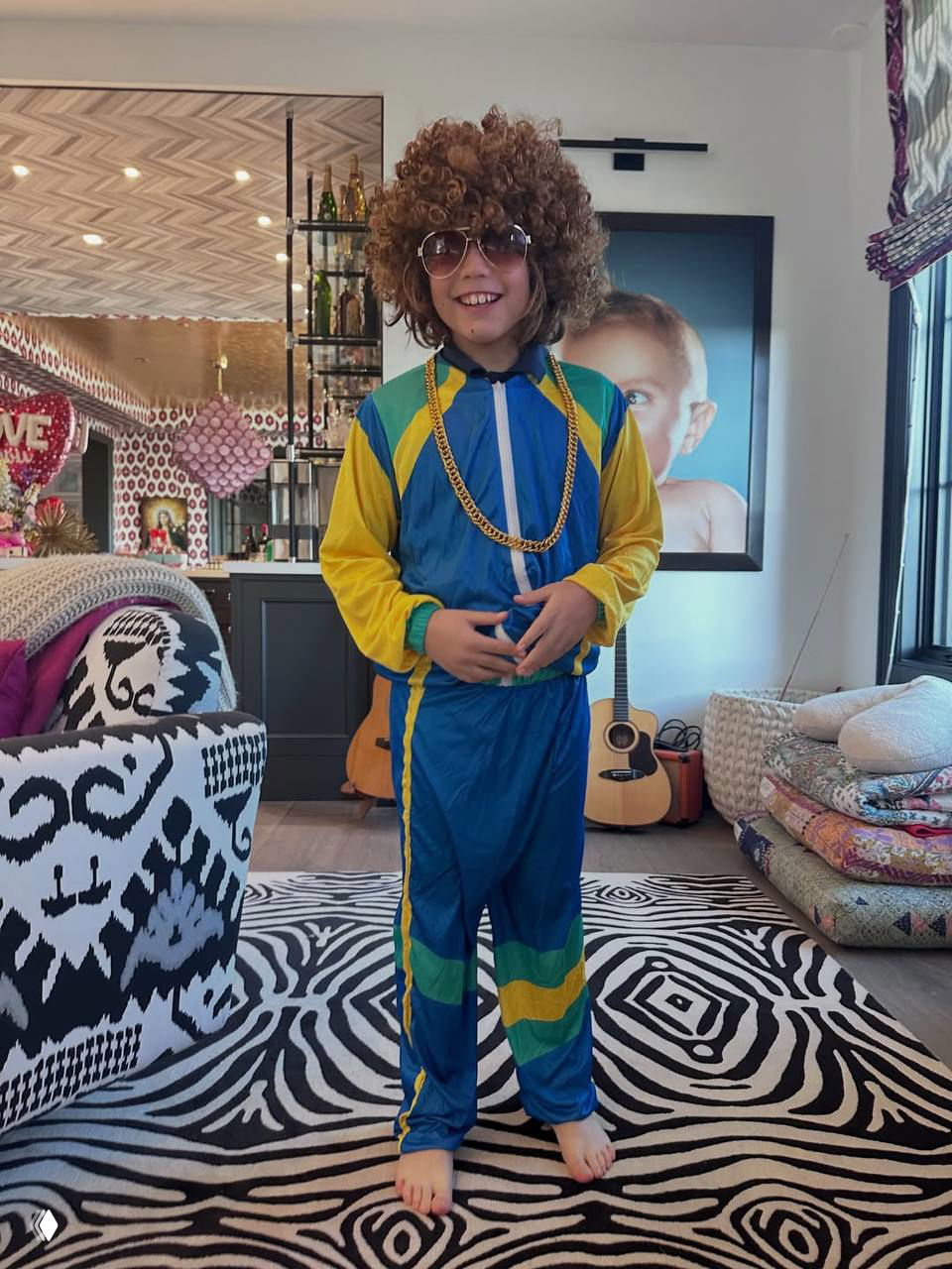 Мальчик в ярком костюме и парике позирует в комнате с гитарой на заднем плане — игровой и домашний образ из подборки.