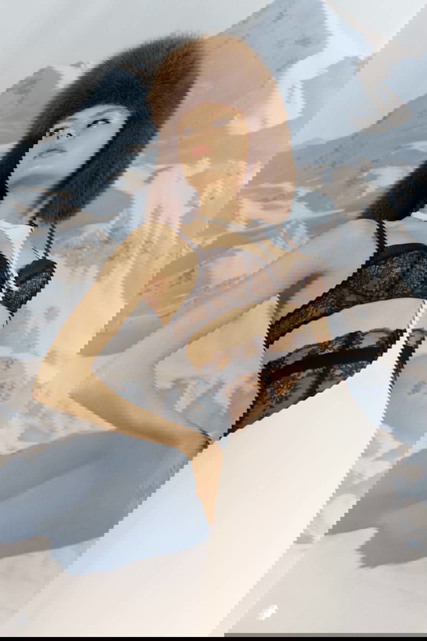 Крупный план ног в ярко‑оранжевых тяжёлых ботинках и красной перчатке на снегу — неожиданный спортивный акцент в гламурной съёмке.