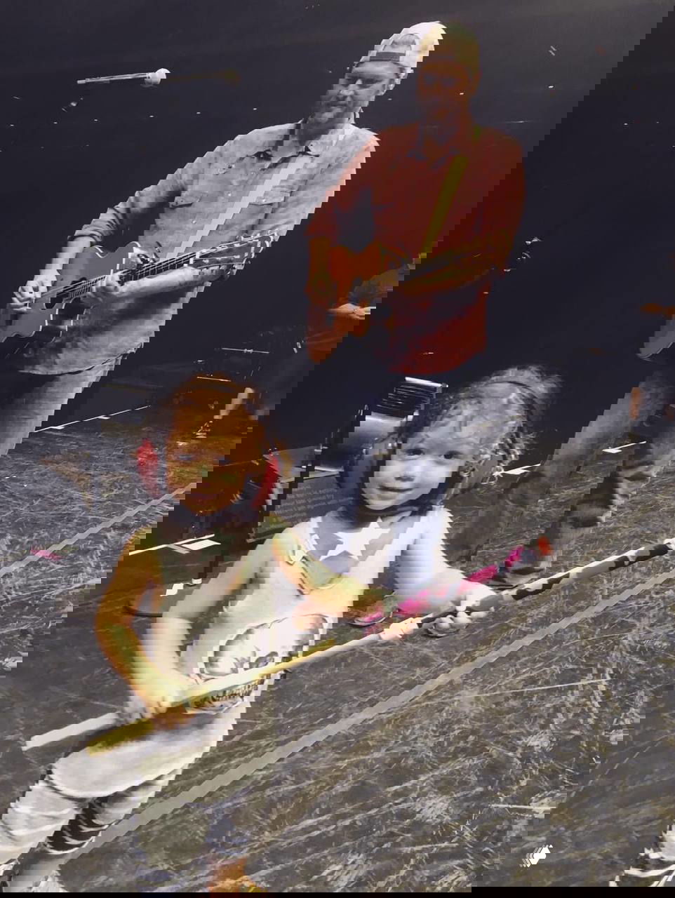 Ребёнок на сцене с берушами и игрушечным реквизитом на фоне оборудования — залипший момент репетиции или представления.