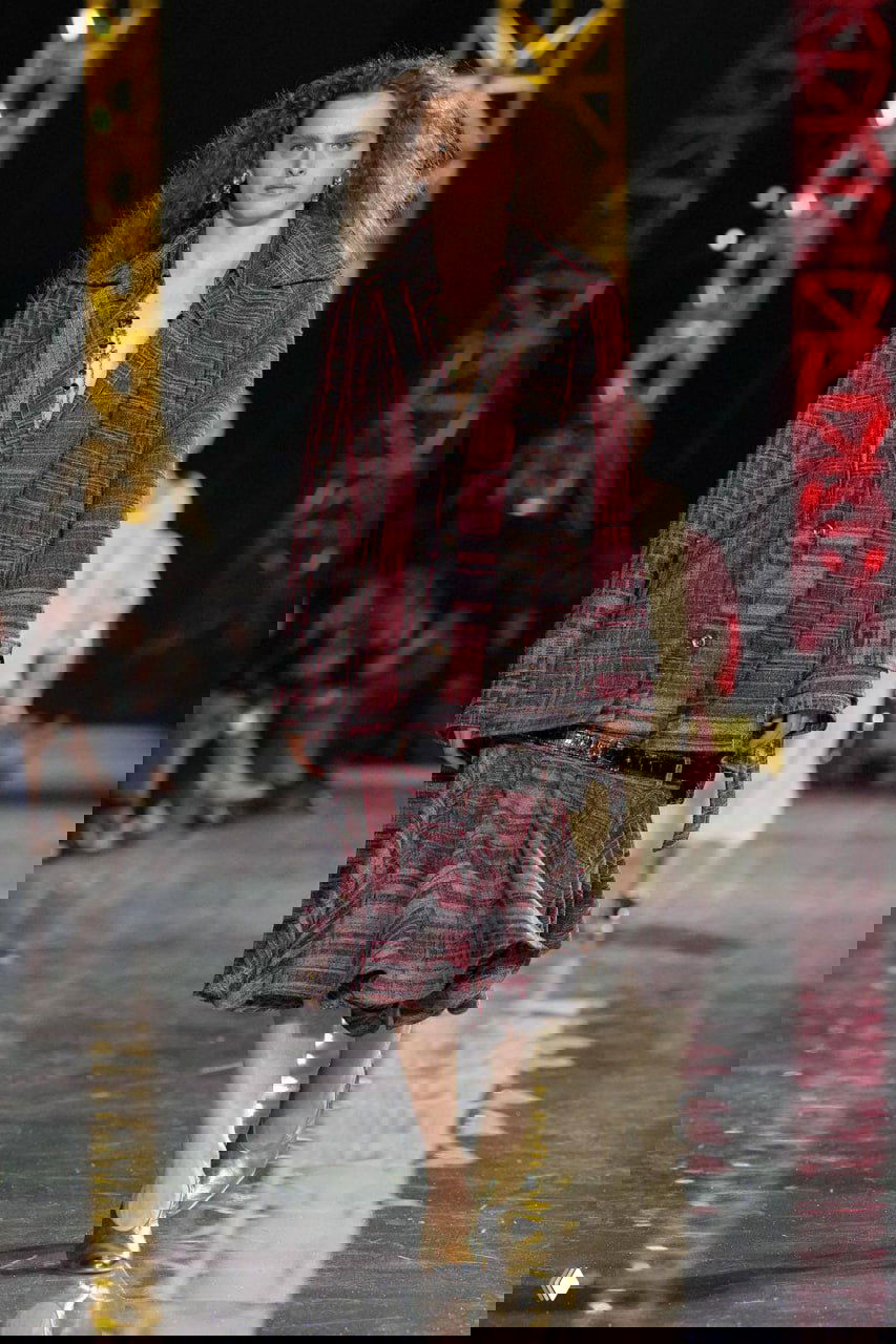 Модель в клетчатом костюме шагает по подиуму, на заднем плане световые конструкции и публика на Парижской неделе моды