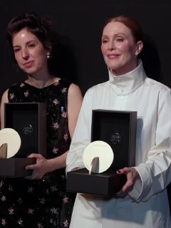Две женщины держат награды на сцене церемонии Women In Motion в Каннах; официальный тёмный фон и статуэтки в руках.