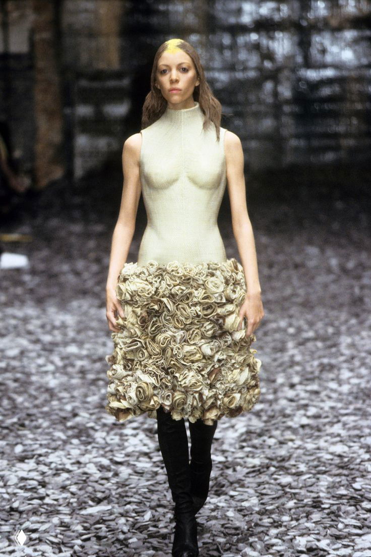 Модель в текстурированной юбке с объёмной цветочной отделкой на фоне естественной подиумной декорации — концептуальный показ начала 2000-х в Париже.