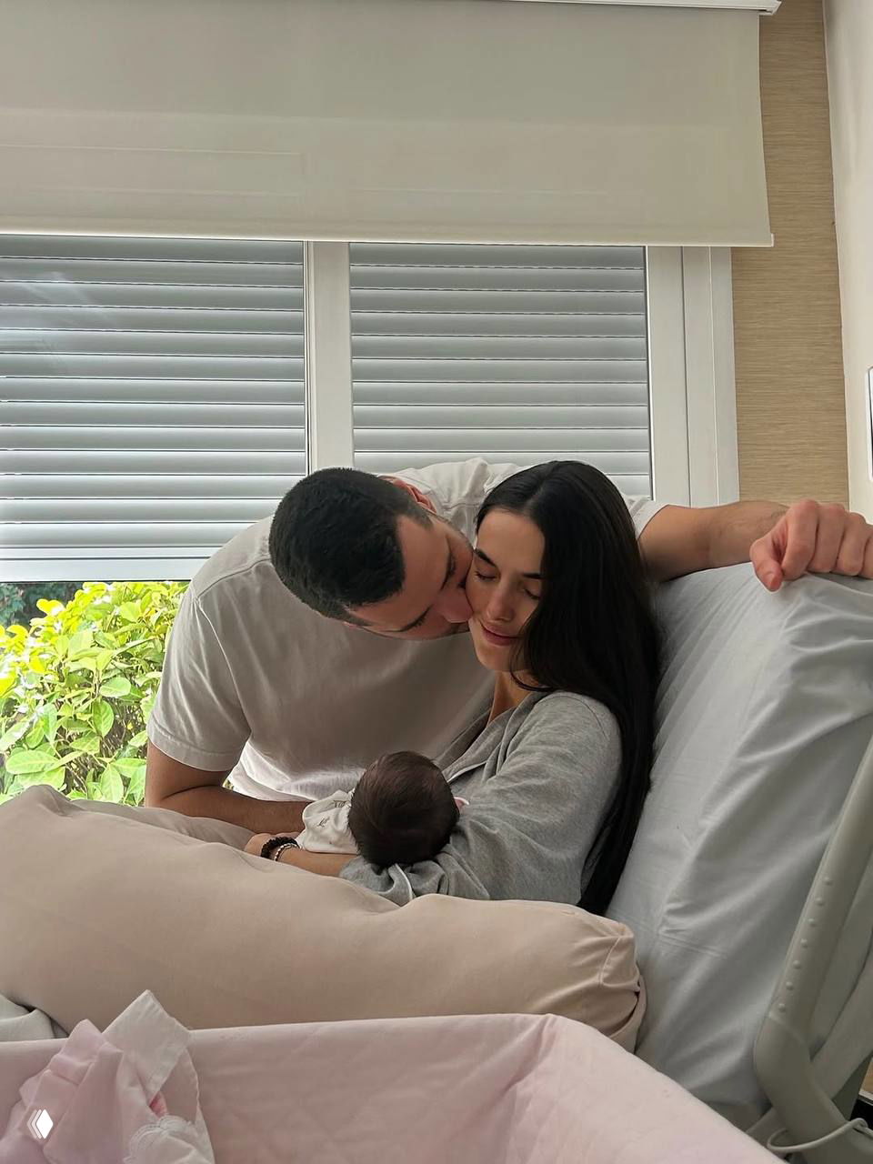 Бланка Падилья и мужчина обнимают друг друга с младенцем на руках у окна — семейный портрет после рождения дочери Майлы.