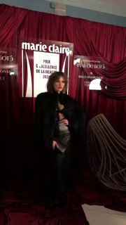 Портрет в тёмном образе на фоне логотипа Marie Claire: насыщенные текстуры ткани и контрастные элементы на бордовой сцене мероприятия.