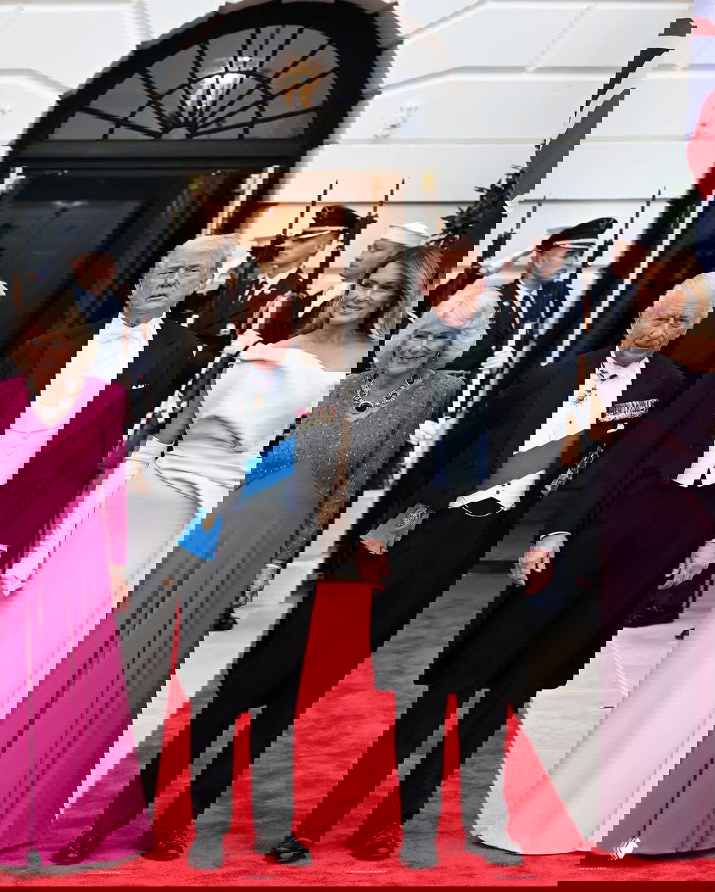 Четверо гостей в вечерних нарядах стоят на красной дорожке перед входом в Белый дом при церемонии с военным эскортом.