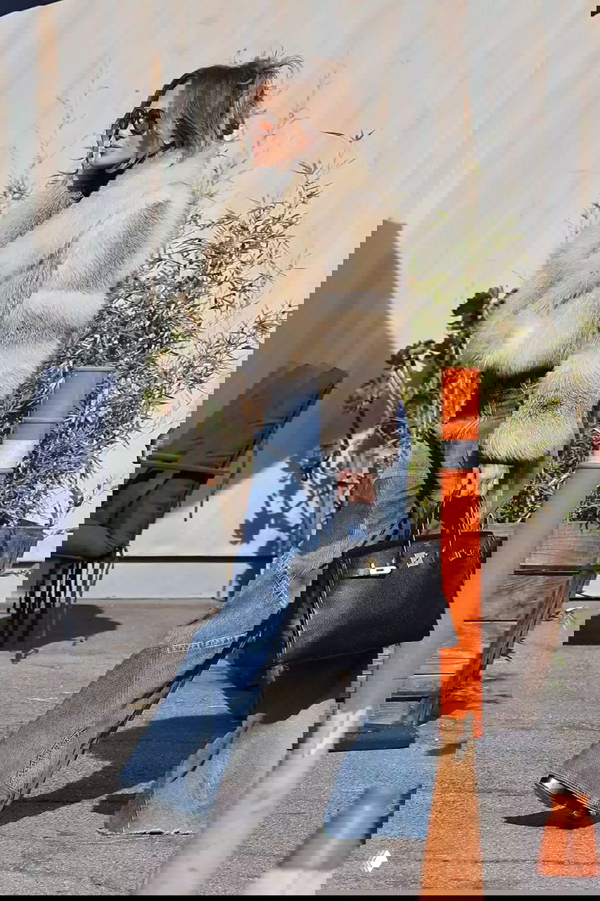 Короткая коричнево‑рыжая шуба в сочетании с клёшеными джинсами и сумкой, уличный дневной кадр при солнечной погоде.